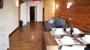 Una habitación con paneles de madera, una mesa de comedor para cuatro personas, un sofá gris y un aparador blanco.