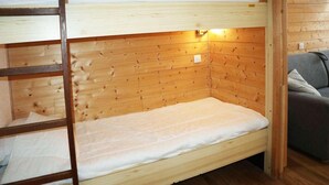 Una cama litera con cabecera de madera y una cama individual debajo. Hay una pequeña lámpara de pared sobre la cama individual.