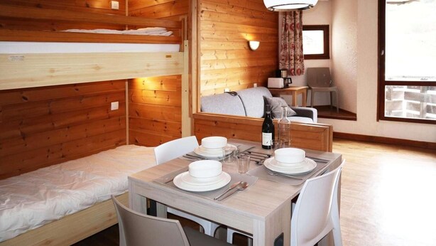 A cozy cabin-style room with a bunk bed, a dining table set for two, a small kitchenette, and a window with curtains. - 100m from ski slopes, 4th floor, balcony, tv, ski locker, 25m², Les Orres (Les Orres)