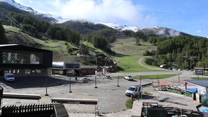 A mountain town with a building featuring a honeycomb facade, a parking area, and a view of snow-capped mountains. - 100m from ski slopes, 4th floor, balcony, tv, ski locker, 25m², Les Orres (Les Orres)