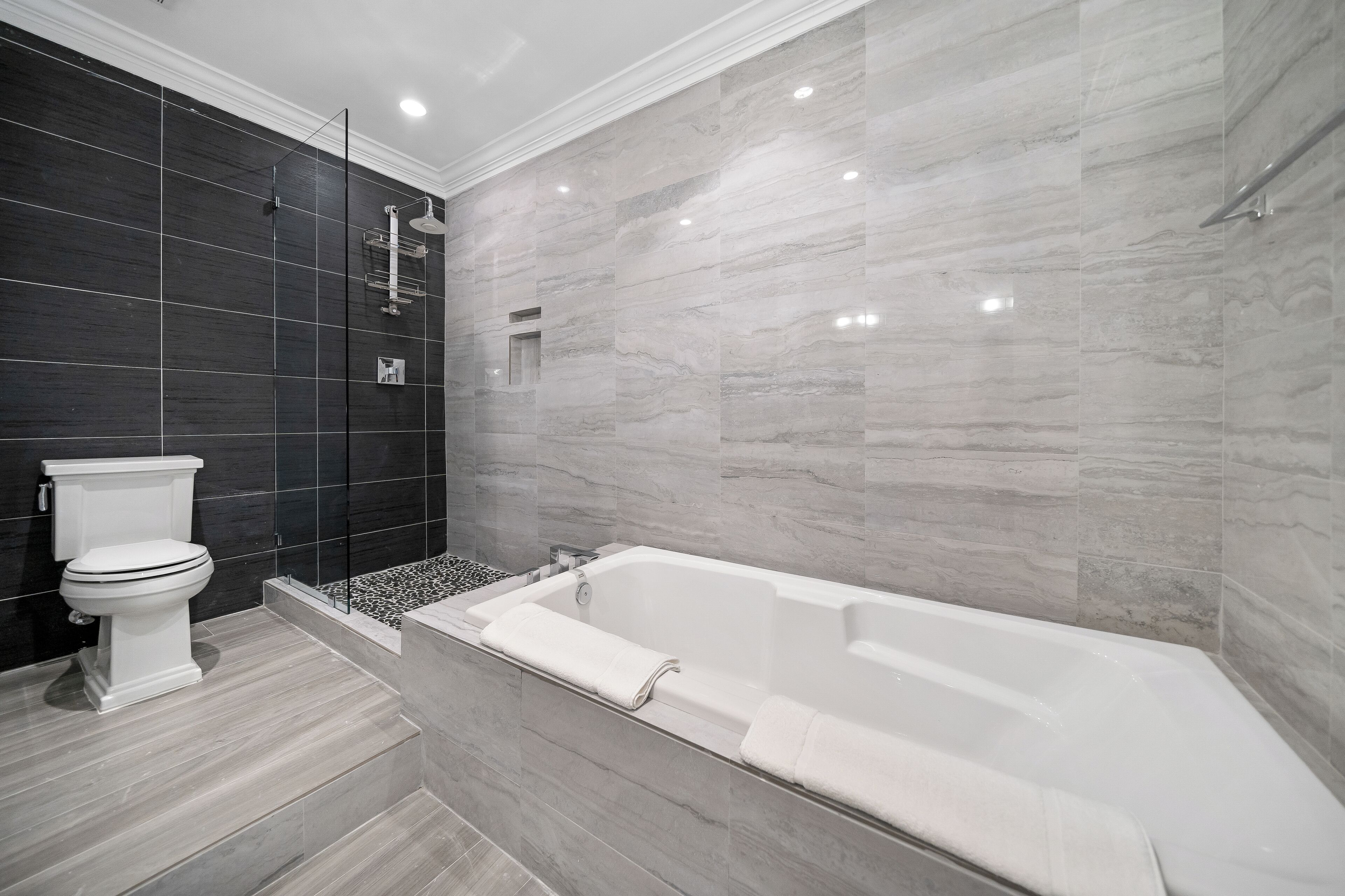 A modern bathroom with a white bathtub, a toilet, and a shower area.