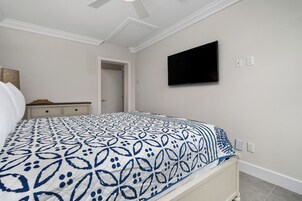 A bedroom with a bed, a TV mounted on the wall, and a door leading to another room.