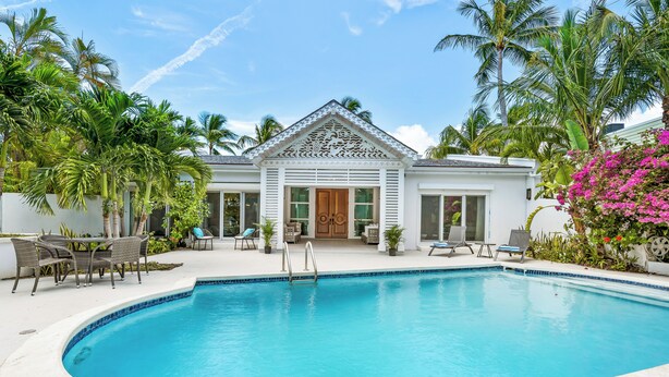 A pool area with a white building, palm trees, and lounge chairs. - Orchid House (Paradise Island)