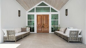 A spacious entryway with a wooden door, two wicker sofas with cushions, and a tiled floor. - Orchid House (Paradise Island)