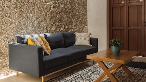 Une pièce avec un mur en pierre, un canapé sombre agrémenté de coussins, une table basse en bois et une porte en bois.