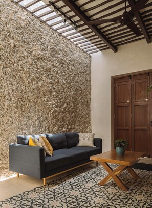 A room with a stone wall, a dark sofa with cushions, a wooden coffee table, and a wooden door. - Spacious 1-floor House, Outdoor Oasis in Centro (Mérida)
