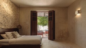Une chambre à coucher avec un lit, une table de chevet et une vue sur un espace extérieur aménagé, visible à travers une porte ouverte.