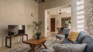 Un salon avec un téléviseur, une table basse en bois, un canapé bleu, un tapis à motifs et une plante.