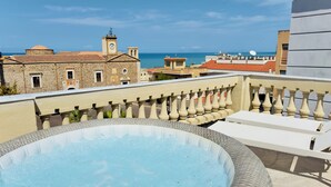 Une piscine sur le toit offrant une vue sur la mer, des bâtiments en pierre et un clocher.