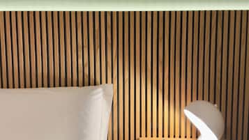 A neatly made bed with pillows, a bedside table with a lamp and a book, and a framed leaf on the wall.