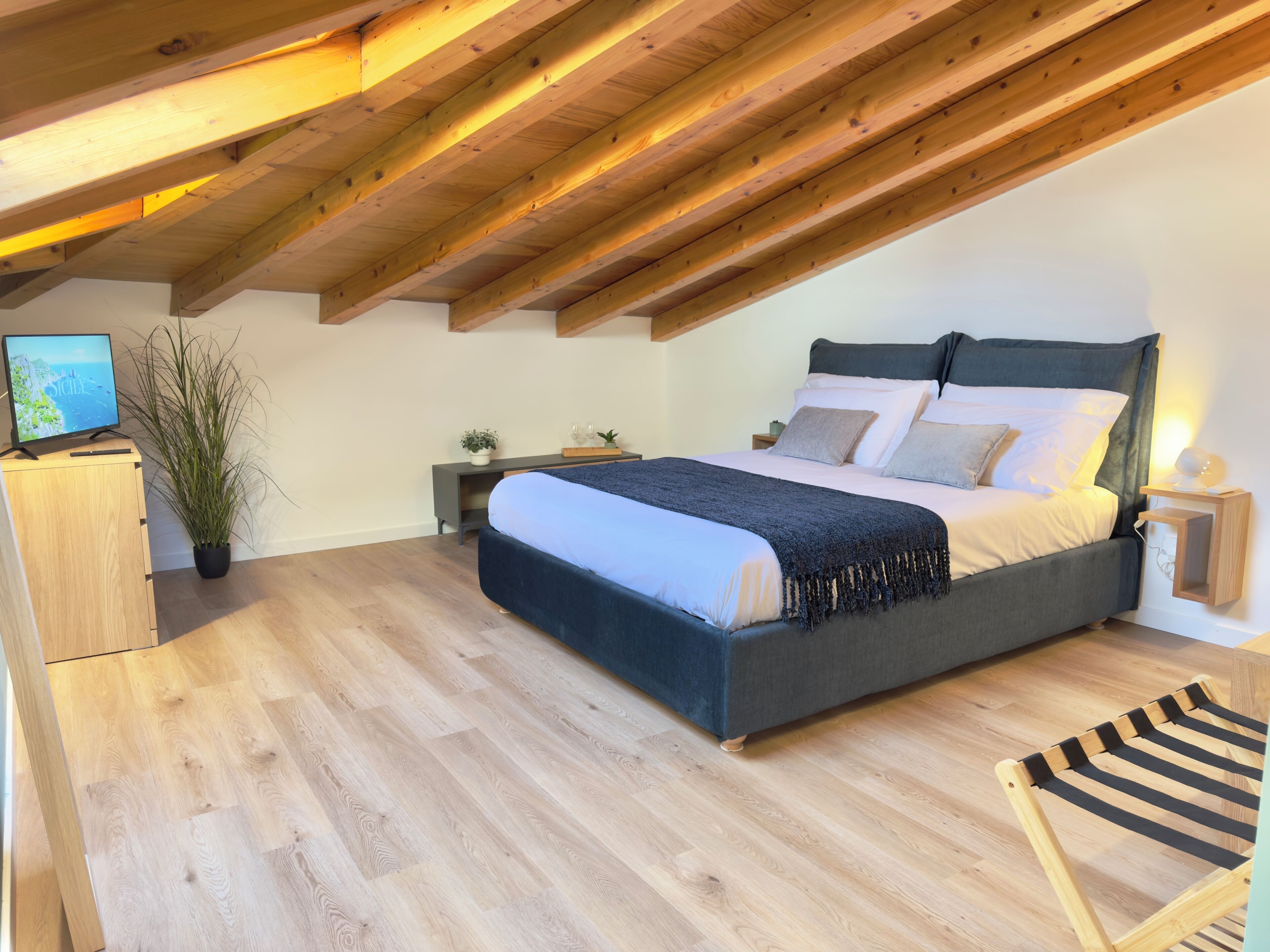 Une chambre avec un plafond en bois, un lit avec une tête de lit sombre, une table de chevet, une commode, un téléviseur et une chaise.
