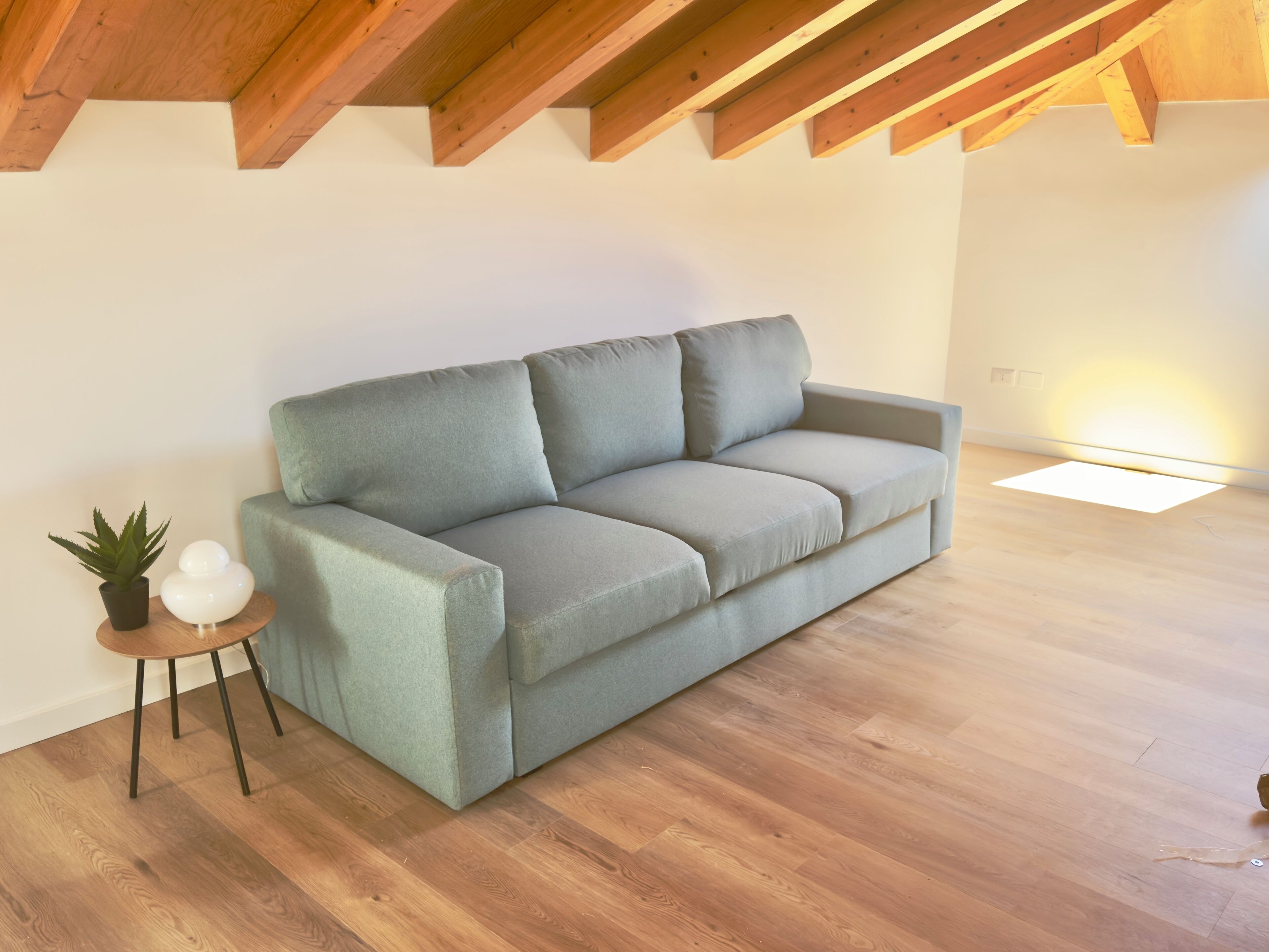 A modern living room with a grey sofa, a small side table with a plant, and a wooden floor.