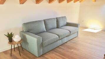 A modern living room with a grey sofa, a small side table with a plant, and a wooden floor.