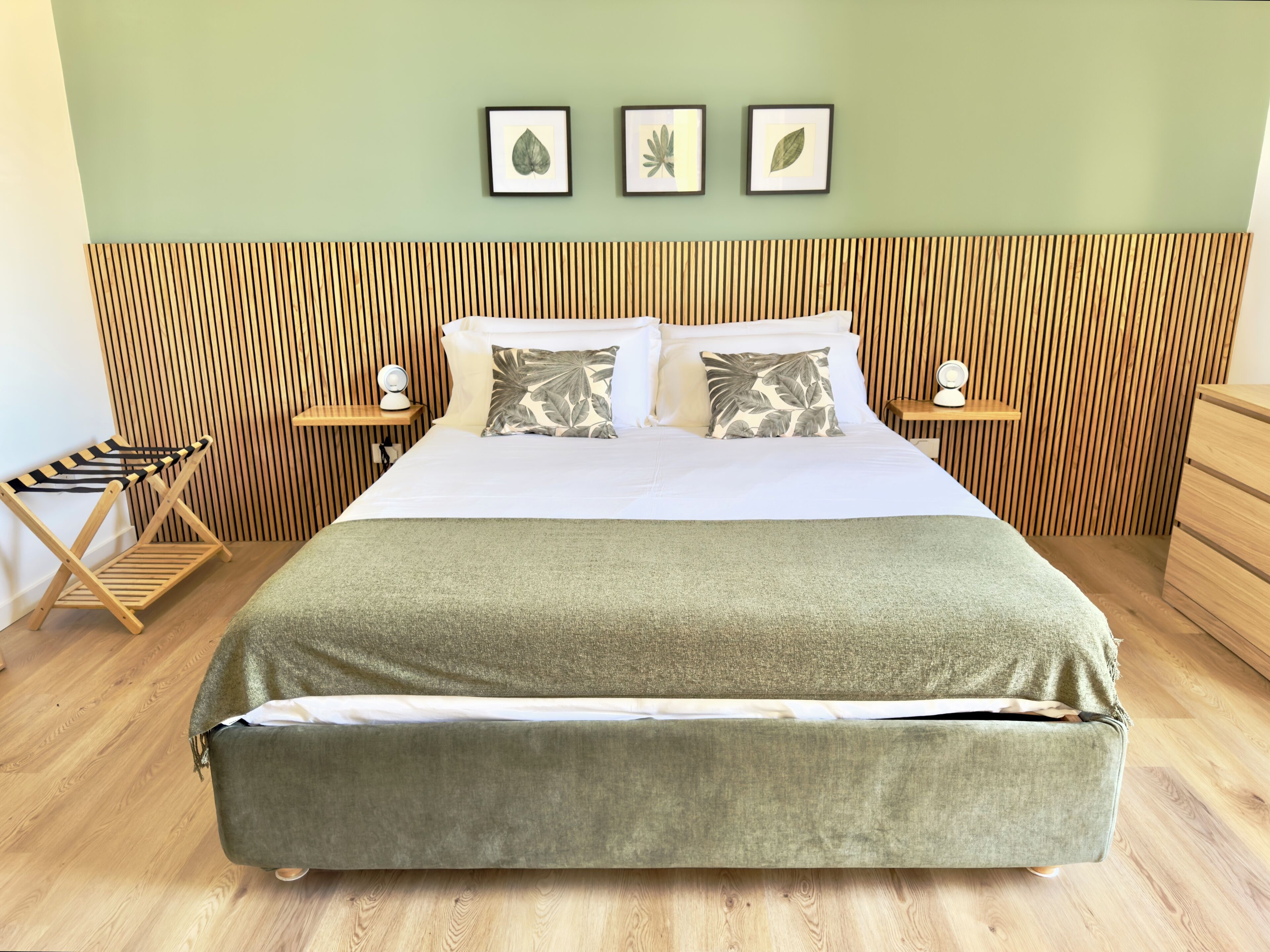 A neatly arranged bedroom with a bed, two bedside tables, a wooden headboard, and a green blanket.