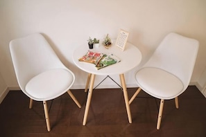 Een witte tafel met twee witte stoelen, een tijdschrift, een klein plantje en een lijst met een afbeelding.