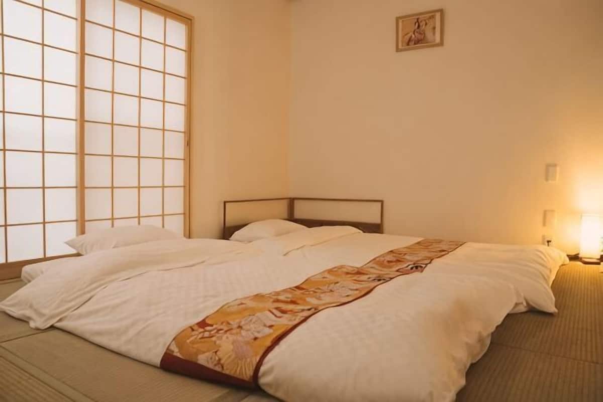 Ein Zimmer mit einem Bett, einem Fenster mit Gittermuster und einem an der Wand hängenden Bild.