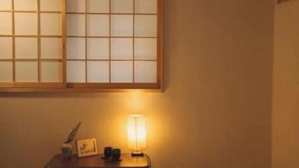 Ein Zimmer mit einer traditionellen japanischen Shoji-Schiebetür, einem kleinen Tisch mit Lampe und einem Bilderrahmen.