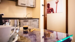 Una cuina amb un taulell, una tassa de cafè, un got de cafè i una cullera. Hi ha un armari per sobre del taulell i una porta amb un cartell.