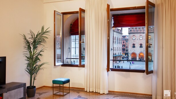 Habitació amb finestra gran que ofereix vista d'un edifici històric i un balcó. Hi ha una planta en test i una panxa propera a la finestra.