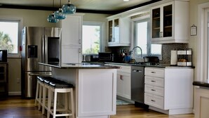 Une cuisine moderne avec des meubles blancs, des appareils en acier inoxydable et un îlot central doté de tabourets de bar.