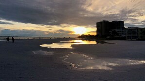 Une plage au coucher du soleil, avec des bâtiments en arrière-plan et un pont.