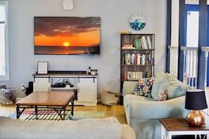 Un salon comprenant un canapé, une table basse, une bibliothèque, un téléviseur fixé au mur et une horloge.