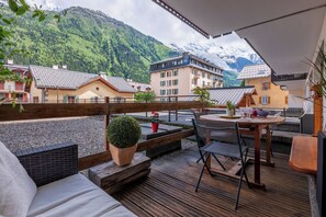 A wooden deck with a table and chairs, overlooking a mountainous landscape with buildings. - In the center of Chamonix with views of Mont Blanc (Chamonix-Mont-Blanc)