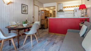 A dining area with a wooden table and chairs, a kitchen with a red accent wall, and a living area with a sofa.