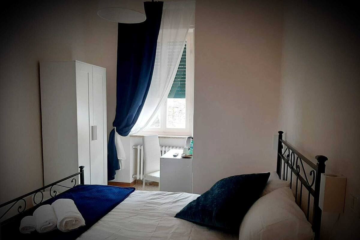 A bedroom with a bed, a radiator, a window with curtains, and a door.