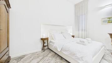 A bedroom with a bed, a nightstand, a wooden wardrobe, and a painting on the wall.