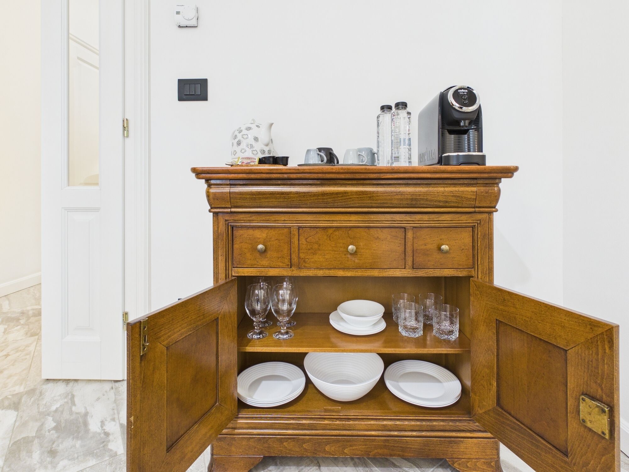 Ein Holzschrank mit Klappe, der weiße Teller, Gläser und eine Kaffeemaschine enthält.