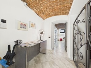 A hallway with a brick ceiling, a desk with papers, a fan, and a metal gate. - ApartHotel No6 (Timisoara)