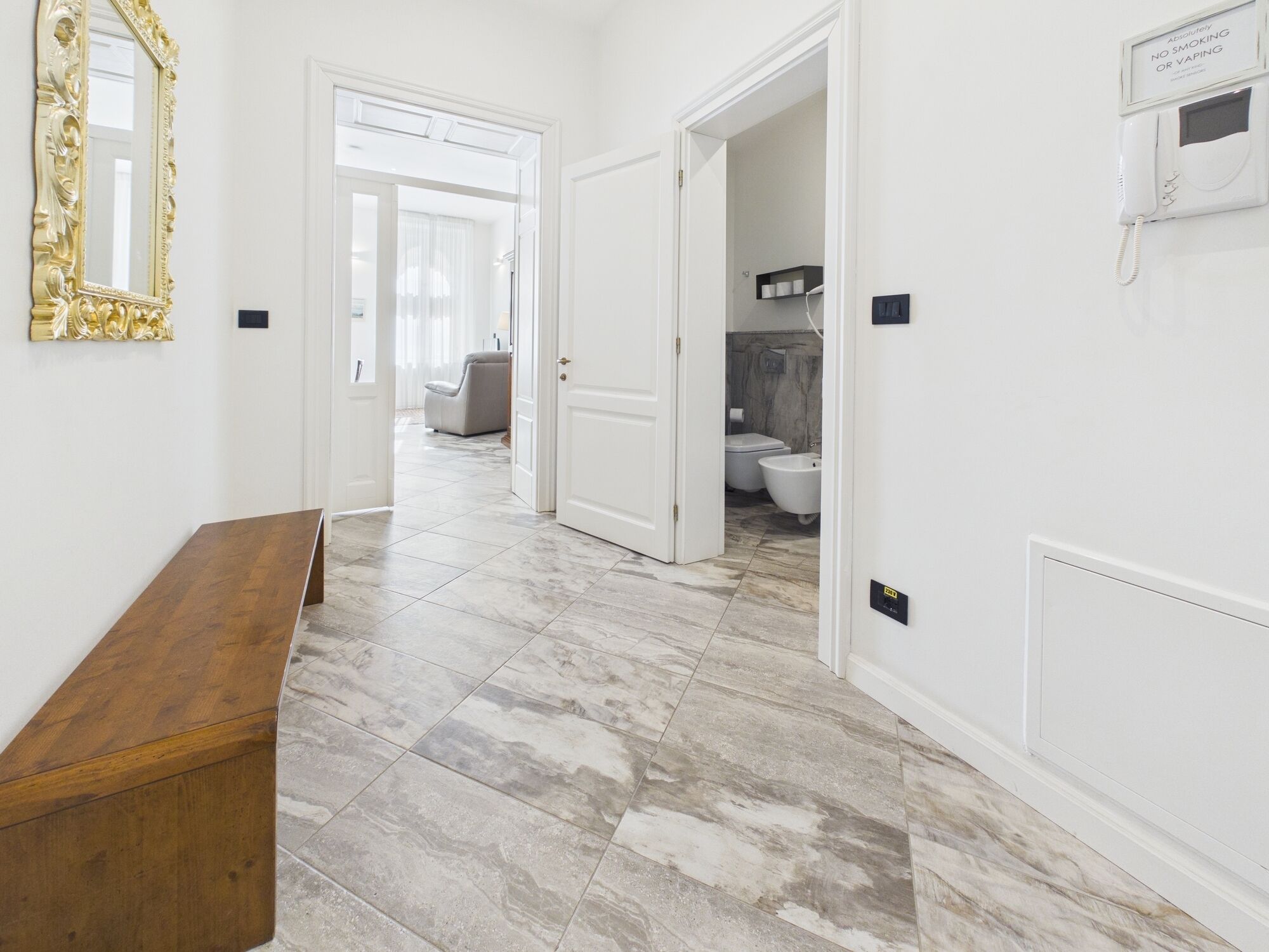 A hallway with a marble floor, a wooden bench, and a white door leading to a bathroom.