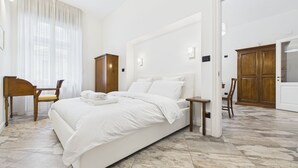 Een hotelkamer met een groot bed, een houten kledingkast, een bureau met stoel en een grote spiegel.