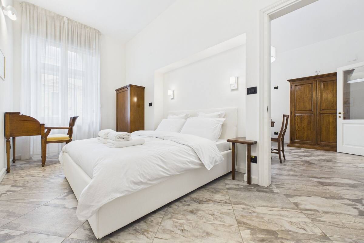 Ein Hotelzimmer mit einem großen Bett, einem Holzschrank, einem Schreibtisch mit Stuhl und einem großen Spiegel.