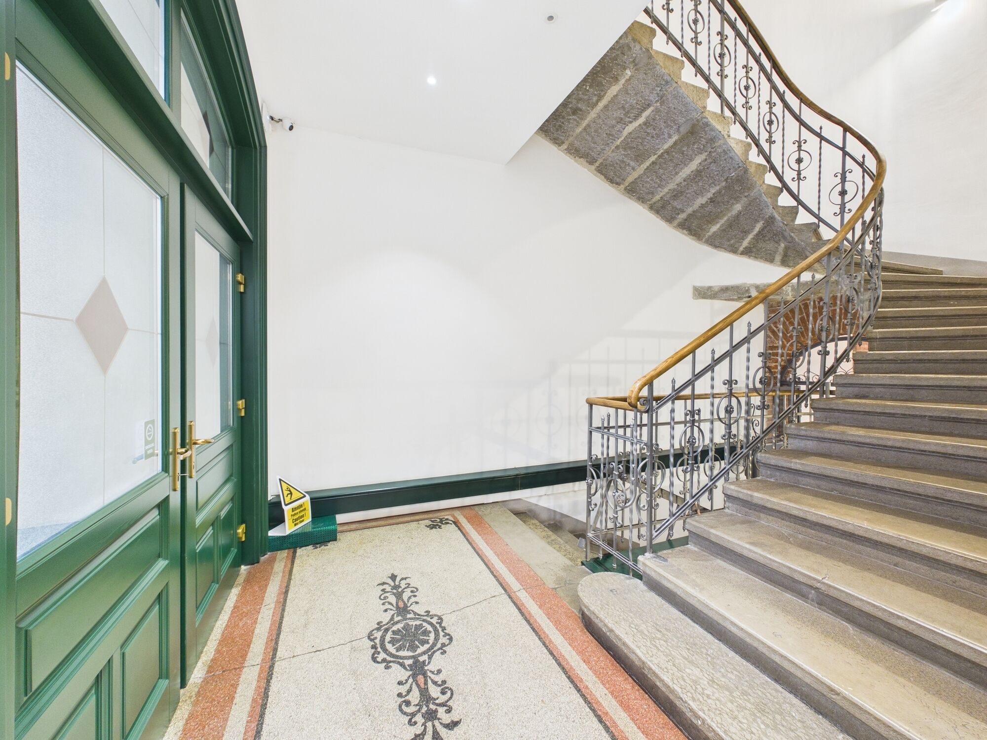 A staircase with ornate metal railings and a wooden handrail, leading to a landing with a patterned floor.