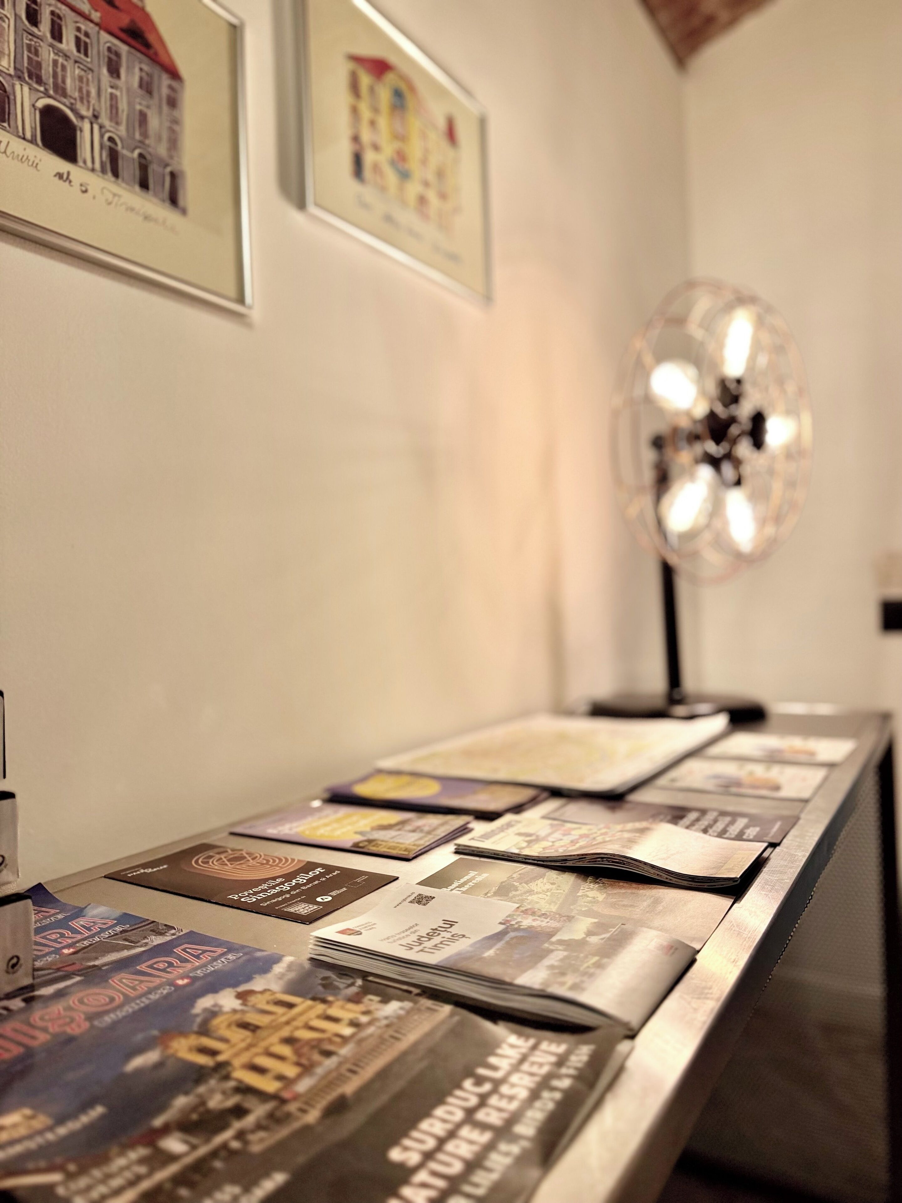 Een receptiebalie met een stapel tijdschriften en brochures, een ingelijste foto van een gebouw, en een decoratieve lamp.
