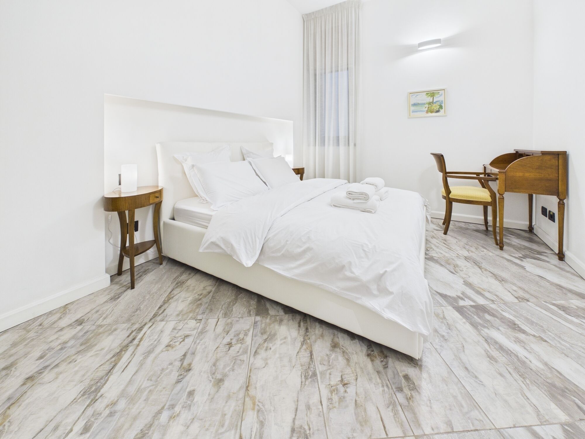 Ein ordentlich eingerichtetes Schlafzimmer mit Bett, Nachttischen, einem Sessel und einem Schreibtisch.