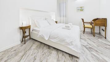 Ein ordentlich eingerichtetes Schlafzimmer mit Bett, Nachttischen, einem Sessel und einem Schreibtisch.