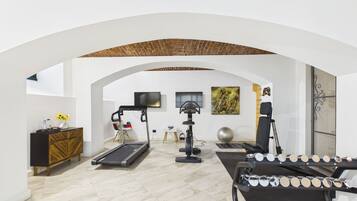 Una habitación amplia con cinta de correr, bicicleta estática y máquina de remo. Hay un televisor montado en la pared y un cuadro decorativo.
