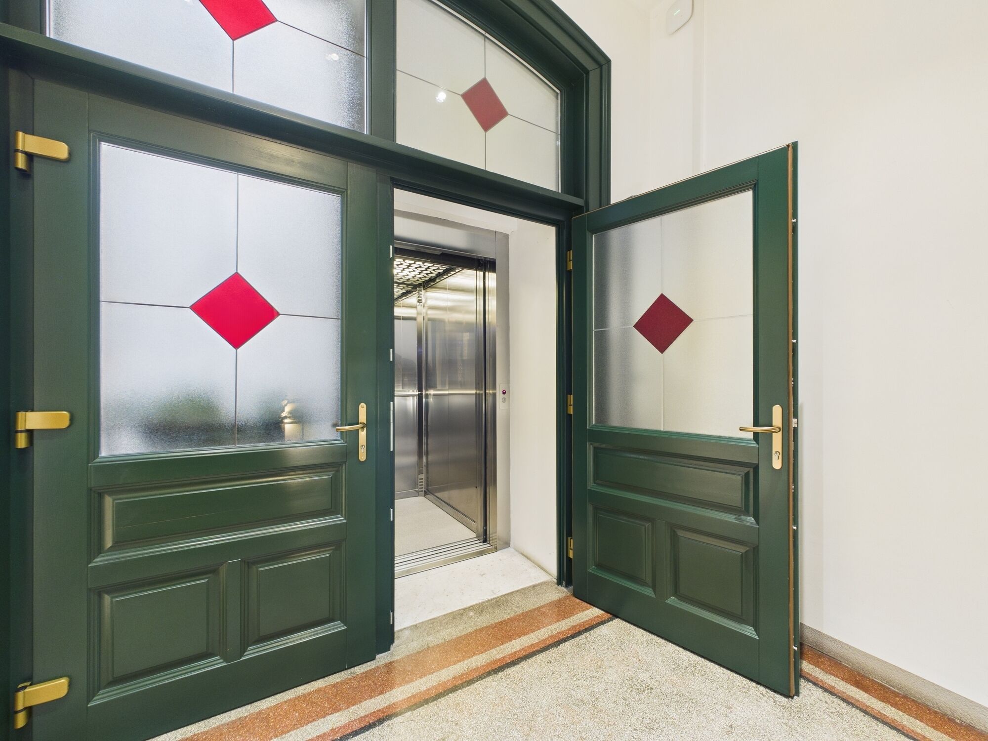 L’entrée d’un hôtel, avec deux portes vertes ornées chacune d’un motif en losange rouge.