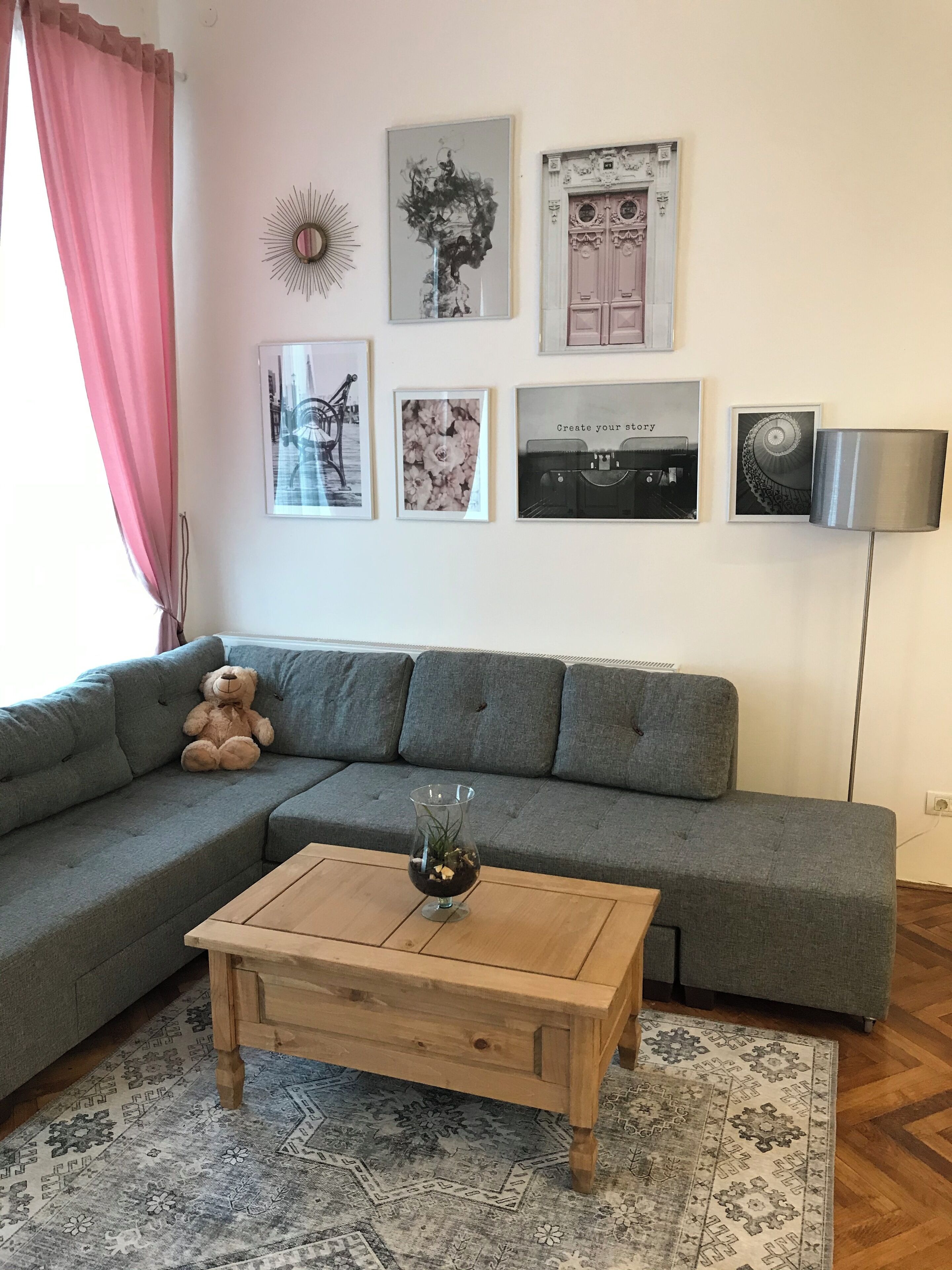 A living room with a grey sectional sofa, a wooden coffee table, a bear plush toy, and a patterned rug.