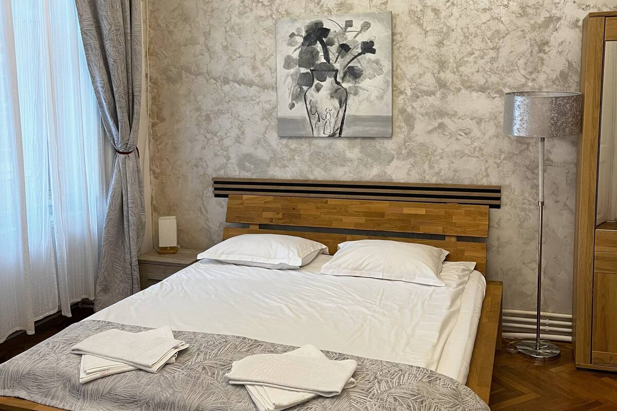 A neatly made bed with white linens, a wooden headboard, and a patterned throw blanket.