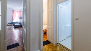Een gang die leidt naar een slaapkamer met een houten vloer, een bed met een roze deken en een nachtkastje.