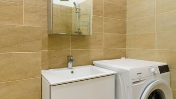 Un baño moderno con baldosas color beige, un lavamanos blanco con un espejo encima y una lavadora de carga frontal.