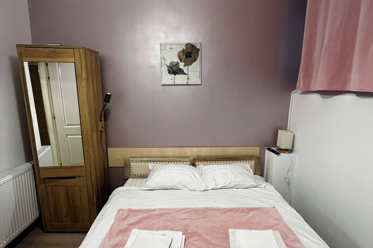 A neatly made bed with pink towels, a wooden wardrobe, a mirror, and a wall-mounted picture.