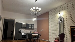 Een moderne keuken met donkere kastjes, een eethoek met een houten tafel en stoelen, en een kroonluchter.