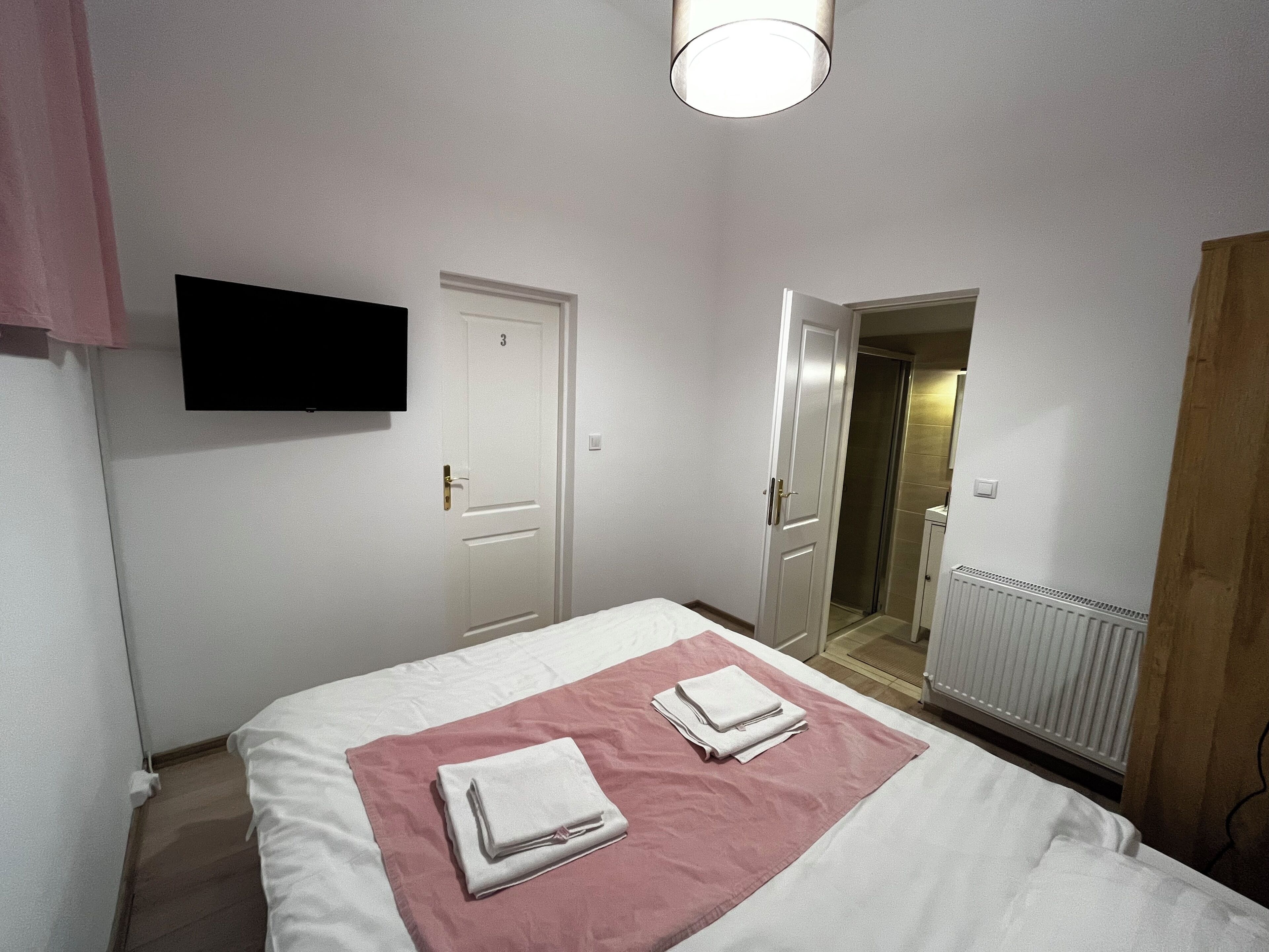 A bedroom with a bed, a pink towel, a white door, a shower, and a radiator.