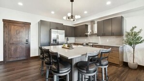 A modern kitchen with a central island, bar stools, and a large wooden door.