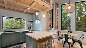 A modern kitchen with wooden cabinets, a central island, bar stools, and a dining table. - Tree House- Two bedroom plus loft- sustainable living! (Bellingham)